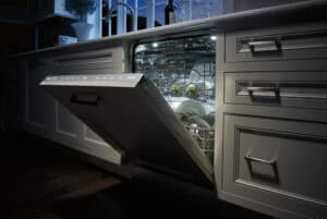 A modern dishwasher with the door open is filled with clean dishes and utensils in a well-lit kitchen at dusk, showcasing a luxury kitchen appliance that elevates the space’s style and functionality.