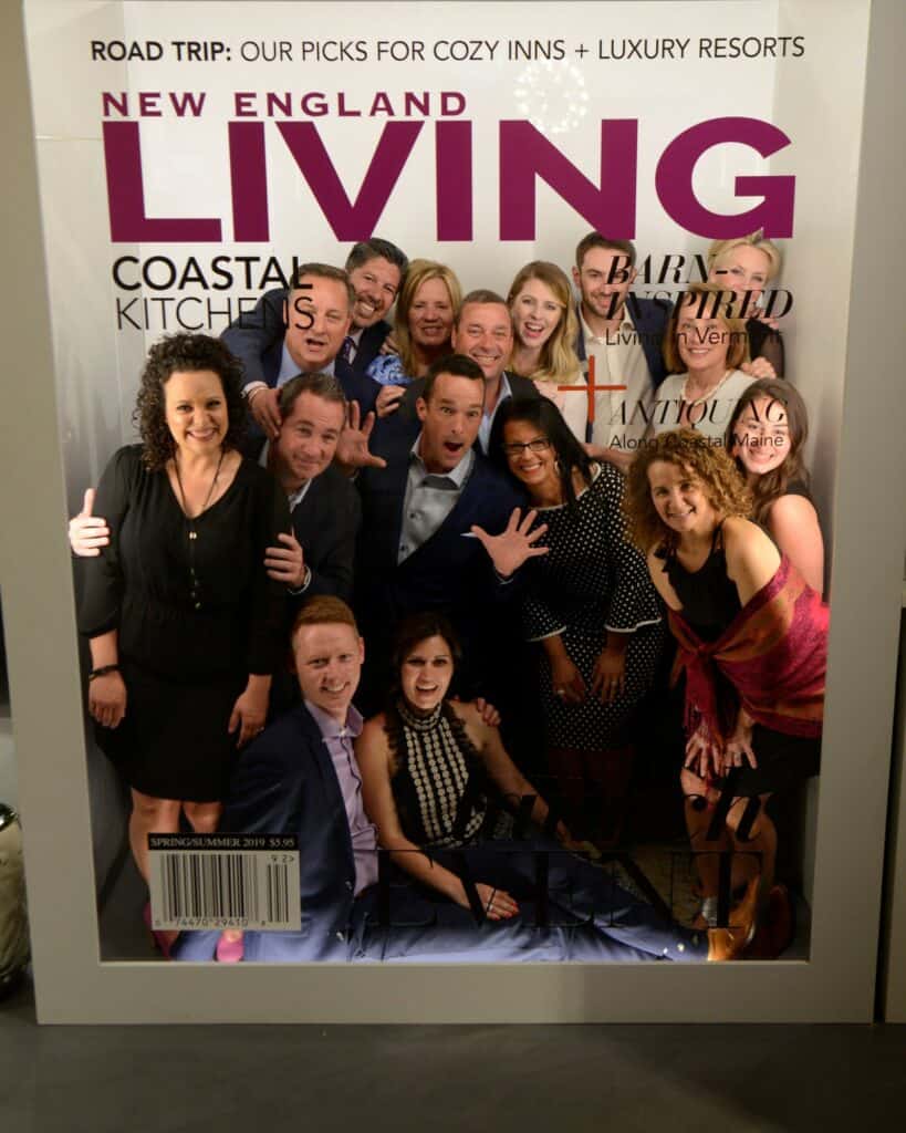 Group of people smiling and posing together for a photo in a stunning kitchen showroom, featured on the cover of New England Living magazine, Fall/Winter 2019 issue.