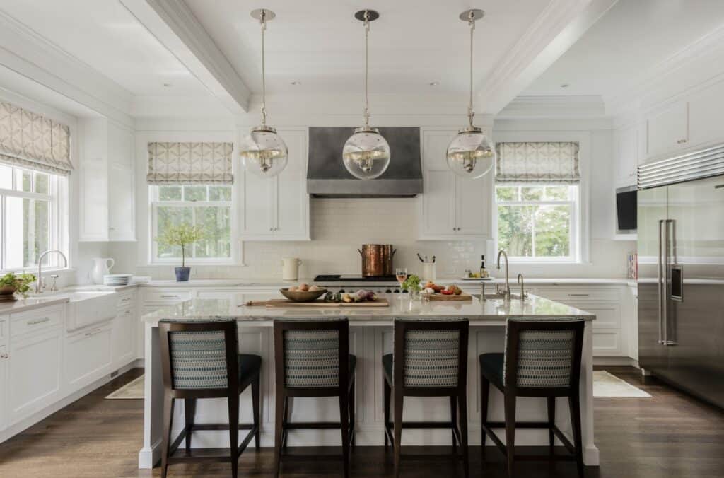 Spacious modern kitchen with white cabinets, stainless steel appliances, a Wolf appliance island with four chairs, pendant lights, and large windows.