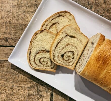 A white rectangular plate with three slices of cinnamon swirl bread and the remaining loaf, on a rustic wooden surface—perfect inspiration for your luxury kitchen appliance collection.