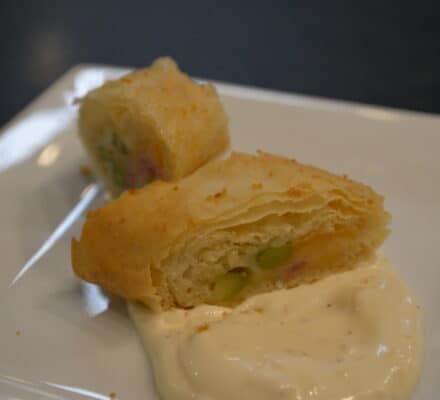 Two pieces of stuffed pastry with a flaky crust are served on a white plate alongside creamy white dipping sauce, perfect for enjoying after exploring the latest designs at your favorite kitchen showroom.