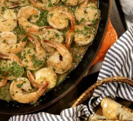Cooked shrimp in a pan with a parsley garnish, served next to sliced bread in a basket with a striped cloth—perfect for showcasing in a kitchen showroom featuring Sub Zero and Wolf appliances.