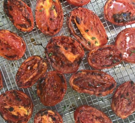 Halved, roasted tomatoes with charred edges are arranged on a metal cooling rack over a baking sheet—perfect inspiration for your next visit to a kitchen showroom.