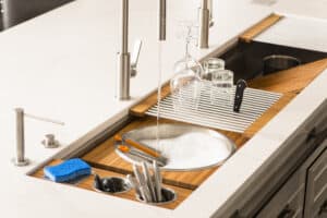 Modern kitchen sink with running water, dishes and glasses drying on a rack, soap dispenser, blue sponge, and utensils in a holder on a clean countertop—perfect for any home with Sub Zero or Wolf appliances from your favorite appliance showroom.