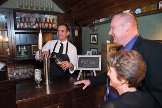 A bartender pours a drink for two smiling patrons at a bar, while a small chalkboard behind the counter displays "Fáilte" beside a sleek sub zero appliance, adding an air of luxury kitchen appliance style to the scene.