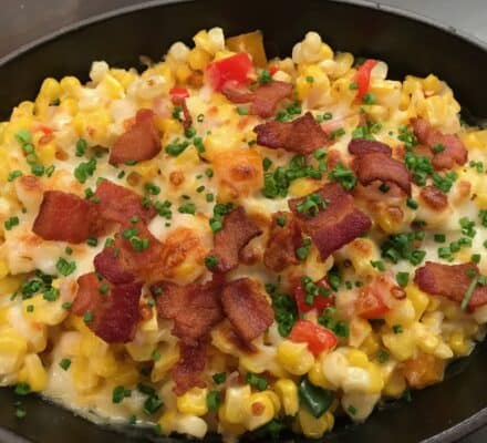 A skillet filled with creamy corn casserole, topped with crispy bacon pieces, diced red peppers, and chopped chives—perfectly cooked using a premium Wolf appliance.