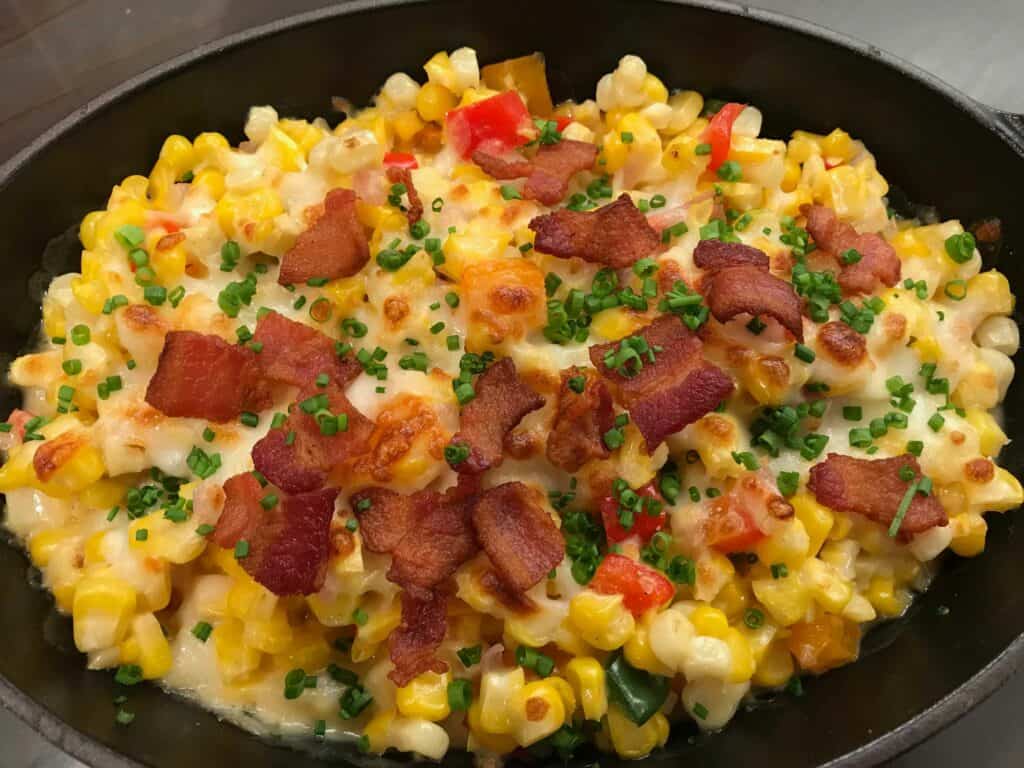 A skillet filled with macaroni and cheese, corn, diced red peppers, chopped chives, and crispy bacon pieces on top—perfectly prepared using a sub zero appliance in a luxury kitchen.