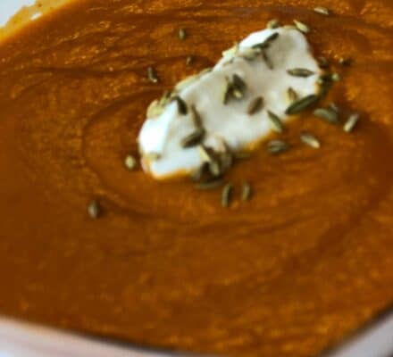 A bowl of creamy orange soup topped with a dollop of cream and sprinkled with seeds, elegantly presented in a white dish—an inspiration for any luxury kitchen appliance display or modern appliance showroom.