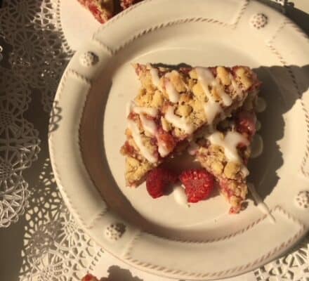 Three triangular pieces of berry crumb bars with icing are arranged on a white plate, set on a decorative lace doily—perfect for serving in an elegant appliance showroom.