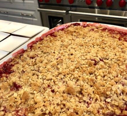 A freshly baked fruit crumble in a white dish sits on a kitchen counter in front of a sleek Wolf appliance, adding warmth and comfort to this luxury kitchen.