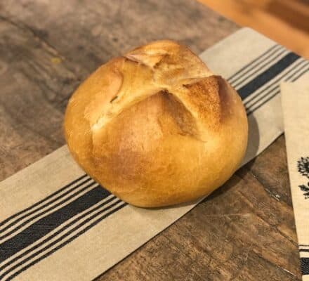 A round loaf of bread with a golden crust sits on a striped cloth atop a rustic wooden table, creating a scene worthy of display in a kitchen showroom.