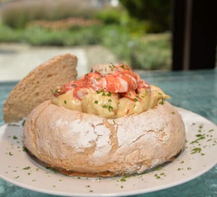 A bread bowl filled with creamy lobster macaroni and cheese, garnished with chopped herbs, sits on a white plate—perfect inspiration for your next meal after visiting a kitchen showroom.
