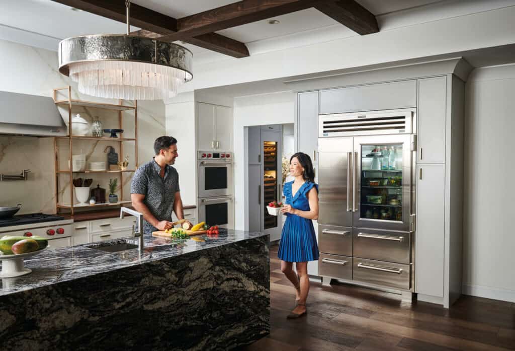 Luxury modern kitchen showroom with stainless steel Sub-Zero and Wolf appliances, custom cabinetry, quartz countertops, and professional-grade gas range under a sleek vent hood.