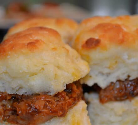 Close-up of two biscuits filled with shredded barbecue meat, with another pair blurred in the background—perfect inspiration for your next meal prepared with a luxury kitchen appliance.