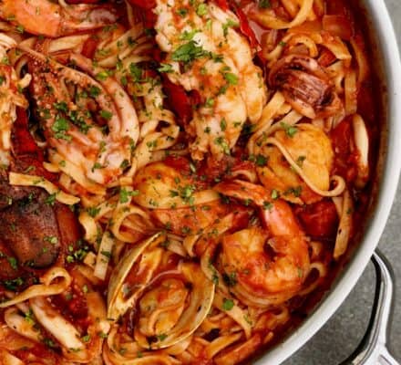 A pan filled with seafood pasta in tomato sauce, featuring shrimp, lobster, clams, and squid, garnished with chopped parsley—an inspiring dish perfect for your next kitchen showroom visit.