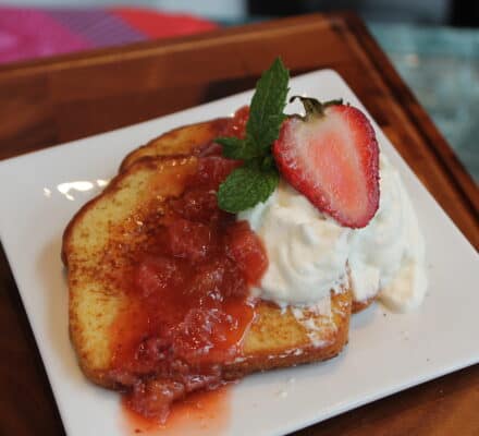 Two slices of pound cake topped with fruit compote, whipped cream, a sliced strawberry, and a mint sprig on a white plate—perfect for serving in any luxury kitchen appliance-inspired setting.