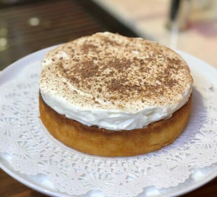 A round cake with whipped cream topping and chocolate sprinkles sits on a white doily atop a cake stand, ready to impress in any appliance showroom featuring the latest Sub Zero appliance displays.