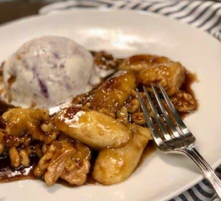 A plate with caramelized bananas and walnuts in sauce, served beside a scoop of ice cream, is beautifully presented—just the kind of dessert you’d imagine preparing after visiting an inspiring kitchen showroom. A fork rests invitingly on the side.