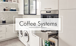Modern kitchen with white cabinets, luxury kitchen appliance, built-in coffee system, pull-out drawer with cups, washer and dryer, and geometric backsplash. Text overlay reads "Coffee Systems.