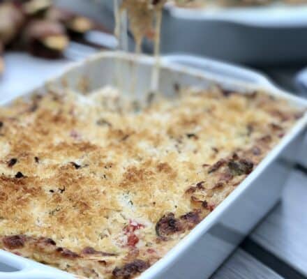 A baked casserole with a golden, crispy topping in a white dish; a serving is being lifted, showing melted cheese—perfect for showcasing in any luxury kitchen appliance display or kitchen showroom.