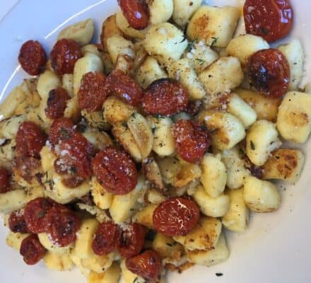 A plate of pan-seared gnocchi topped with roasted cherry tomatoes, grated cheese, and herbs is beautifully presented, perfect for any kitchen showroom display.