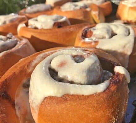 Close-up of freshly baked cinnamon rolls topped with melted icing, arranged closely together on a tray in natural sunlight—perfectly prepared using a luxury kitchen appliance.