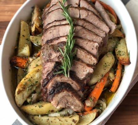 Sliced roast beef garnished with rosemary, served on a bed of roasted potato wedges and carrots in a white oval dish—perfect inspiration for any luxury kitchen appliance display or appliance showroom.