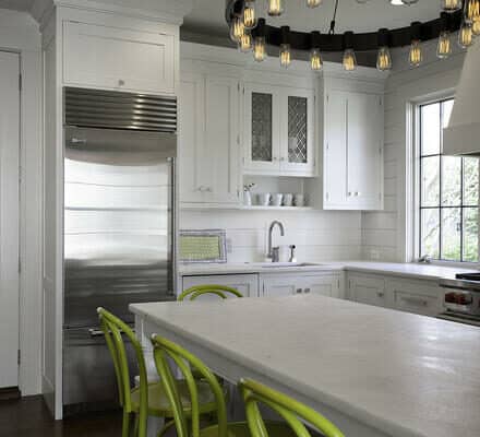 Modern kitchen with white cabinetry, a luxury kitchen appliance package including Wolf appliances, stainless steel accents, a large island, bright green chairs, and a circular chandelier with exposed bulbs.