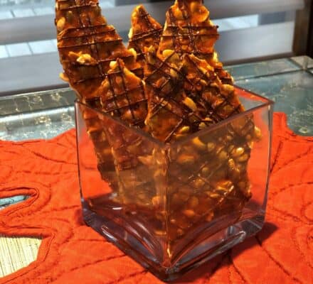 Pieces of nut brittle with a chocolate drizzle stand upright in a square glass container, placed on an orange mat with a leaf pattern—adding sweet elegance to any luxury kitchen appliance showroom display.