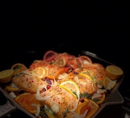 Seasoned salmon fillets topped with lemon and orange slices, herbs, and spices, arranged in a cast iron skillet—perfect inspiration for your kitchen showroom or appliance showroom display.