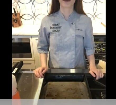 Chef Shelby stands behind a kitchen counter in an appliance showroom, demonstrating griddle cleaning with a dirty griddle tray. Text reads: "Griddle Cleaning With Chef Shelby.