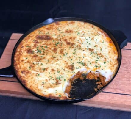 A cast iron skillet with shepherd's pie, topped with browned mashed potatoes and parsley, with a serving scooped out to reveal the meat filling underneath—just like you'd see in a kitchen showroom featuring a gleaming Wolf appliance.