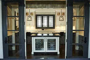 Modern kitchen with glass double doors, a central island featuring glass-front cabinets, pendant lights, white cabinetry, and premium Wolf appliances for a touch of sophistication.