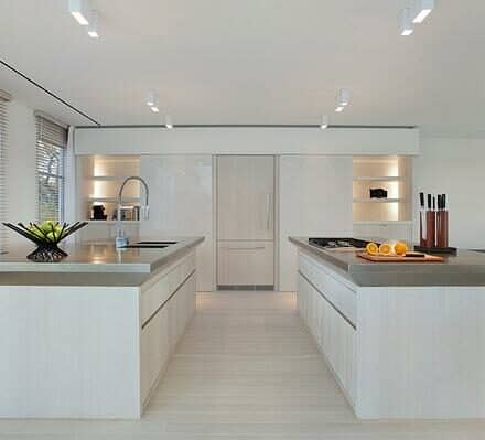 Modern kitchen with two large islands, white cabinetry, stainless steel countertops, built-in Sub Zero appliance, and bright natural light from windows—perfect inspiration for your dream luxury kitchen showroom.