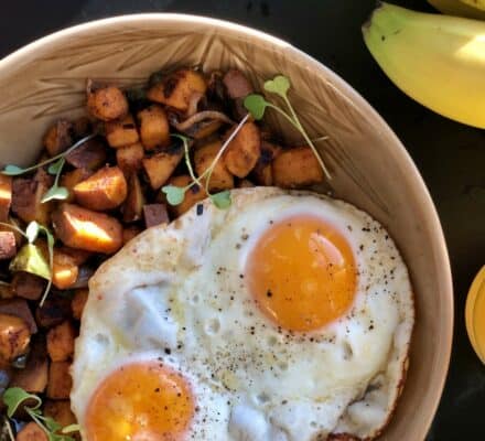 A bowl with two sunny-side-up eggs and sautéed diced potatoes, garnished with microgreens, is displayed—perfect inspiration for a kitchen showroom featuring Wolf appliances. Bananas and a yellow container sit beside the bowl.