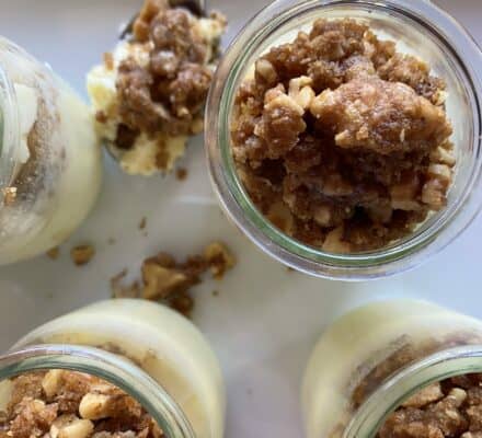 Four glass jars filled with layered dessert featuring creamy custard at the bottom and a crumbly nut topping, with one jar partially eaten and a spoon nearby—perfectly prepared using your favorite luxury kitchen appliance.