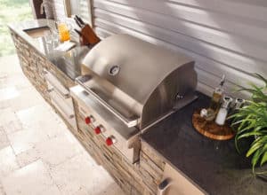 Outdoor kitchen with a stone countertop, built-in stainless steel grill with red knobs, sink, cutting board, and condiments on a wooden tray—just like the setups you’d find in a top kitchen showroom for luxury kitchen appliance inspiration.