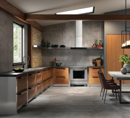 Modern kitchen showroom with wood and gray cabinets, stainless steel appliances—including Sub-Zero appliance—open shelves, a dining table with chairs, large window, and a skylight.