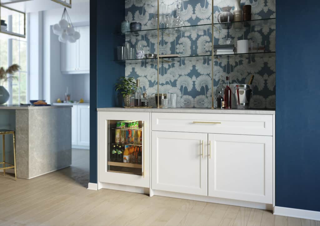Modern home bar area with white cabinets, built-in mini fridge, glass shelves holding bottles and glassware, luxury kitchen appliance touches, and a patterned wallpaper accent.