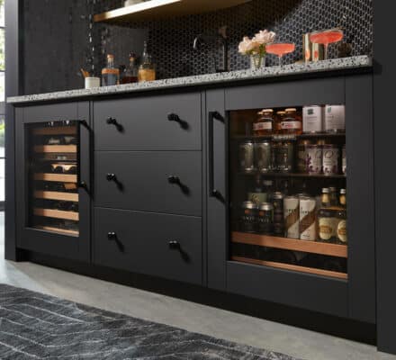A modern black bar cabinet with a granite countertop, glass-fronted wine and beverage coolers, and various bottles and glasses displayed on top—perfect for showcasing in any luxury kitchen appliance showroom.