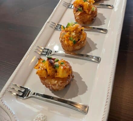 Close-up of crispy rice cakes topped with spicy lobster mixture, garnished with green onions and sesame seeds, served on a white plate