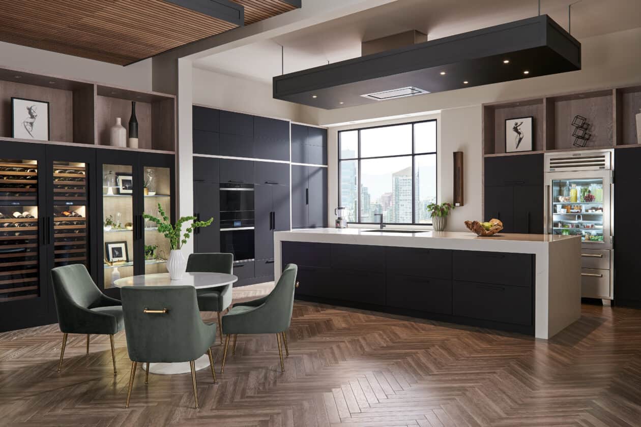 Modern kitchen and dining area with dark cabinets, luxury kitchen appliances, a round table with green chairs, and a large window providing natural light—perfect inspiration for any appliance showroom.