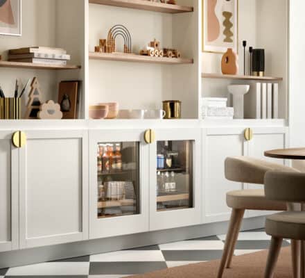 Modern living room with built-in white shelves displaying books, abstract art, and decorative objects, plus a cabinet with glass doors—designed with the elegance of a luxury appliance showroom and featuring a checkered floor near a stylish table and chairs.