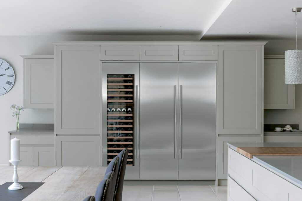 Modern kitchen with built-in Sub-Zero appliance refrigerator and wine cooler, light gray cabinets, a dining table, chairs, and a wall clock—perfect for showcasing luxury in any appliance showroom.