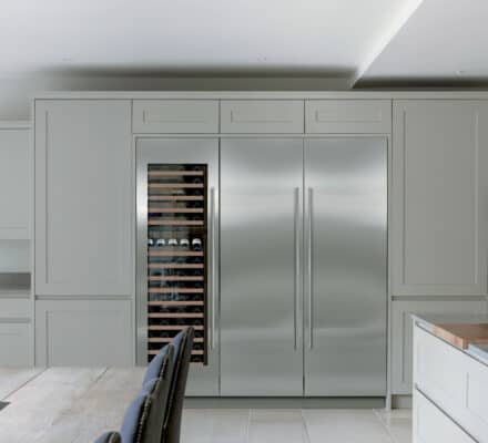 Modern kitchen with built-in Sub-Zero appliance refrigerator and wine cooler, light gray cabinets, a dining table, chairs, and a wall clock—perfect for showcasing luxury in any appliance showroom.