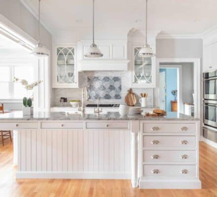Bright, spacious kitchen with white cabinetry, marble island, stainless steel appliances—including a Sub Zero appliance—wooden floors, and pendant lights above the island, perfect for a kitchen showroom display.
