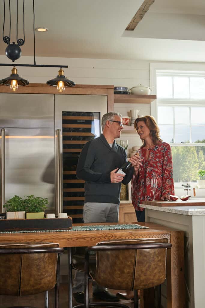 A man and woman stand together in a modern kitchen, smiling at each other near the counter, with natural light coming through a window—showcasing how to add value to your home with stylish upgrades.