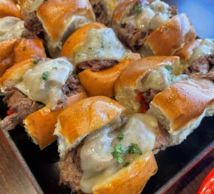 Mini Philly Cheesesteak sandwiches with thinly sliced beef, melted cheese, and sautéed peppers and onions, served on small hoagie rolls, perfect for a tasty appetizer or snack.