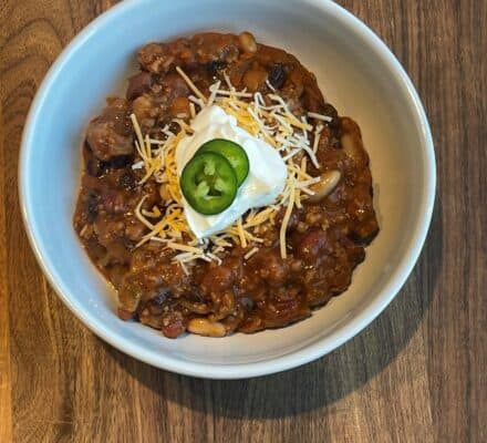 Hearty Super Bowl Chili served in a bowl, topped with shredded cheese, and sour cream, perfect for a game day feast or a comforting meal