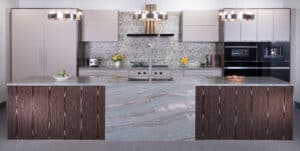 Modern kitchen showroom featuring a large marble island, wood paneling, mosaic tile backsplash, built-in sub zero appliance, and elegant pendant lights.